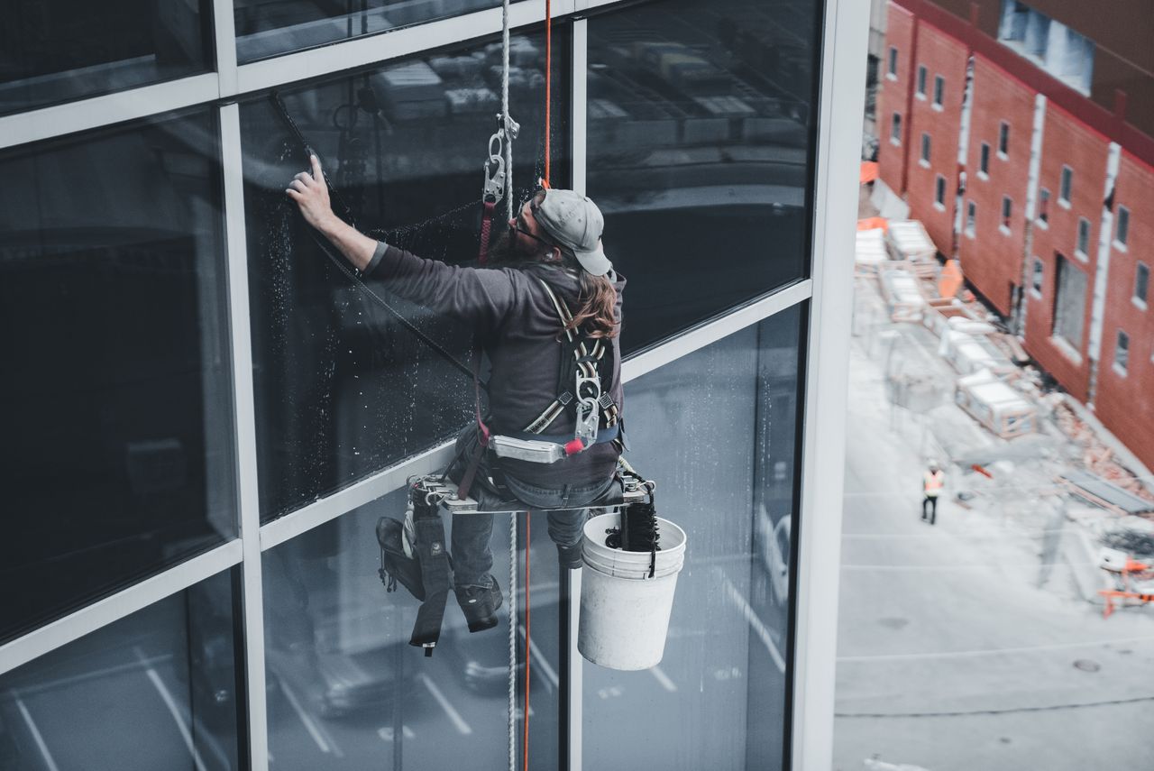 Un ouvrier nettoie les vitres d’un gratte-ciel, harnaché, dans un cadre urbain.